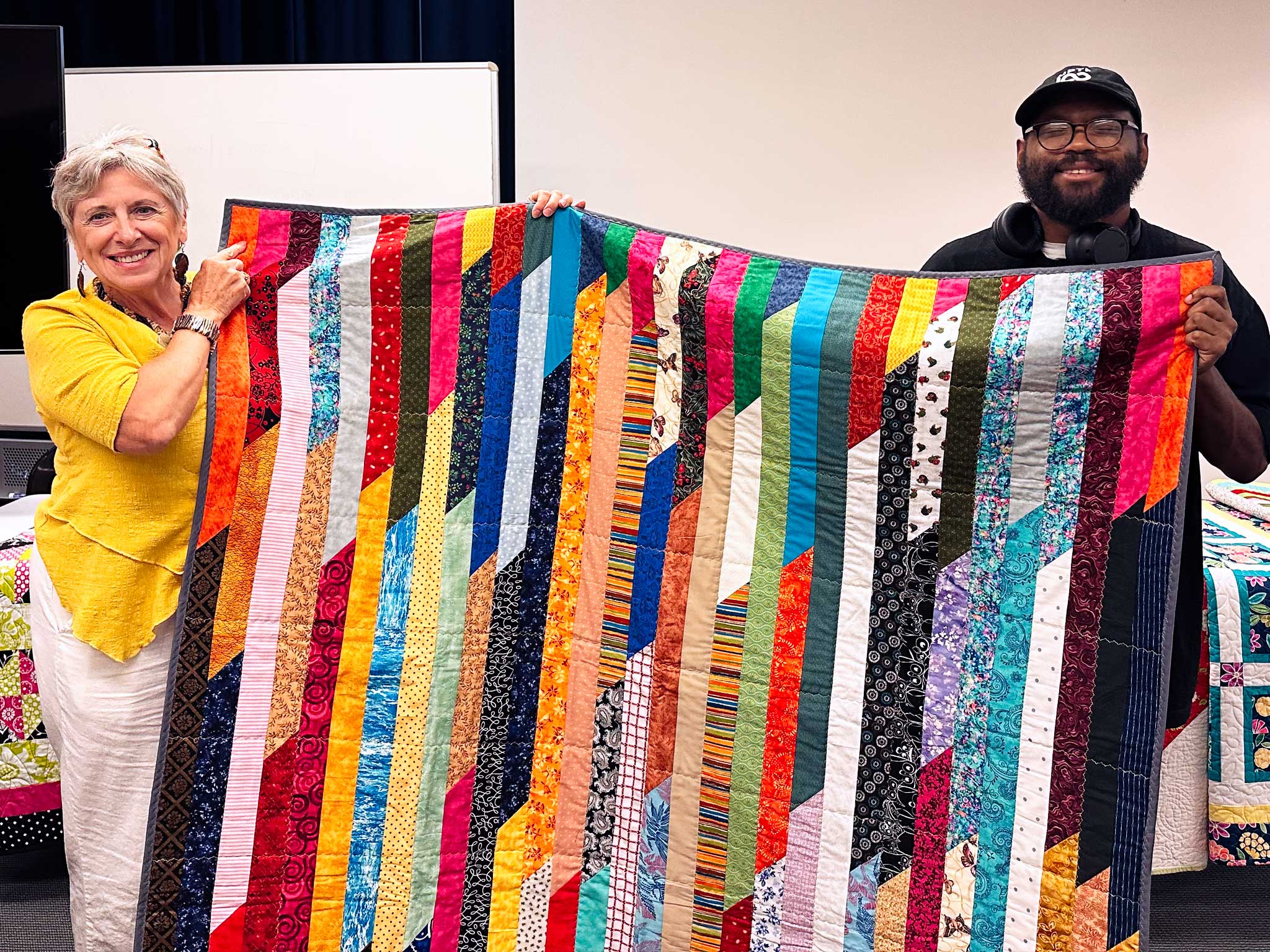 two people hold up a striped quilt